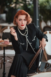 a lady in a black mock nec top, a black jacket and a black pleated skirt